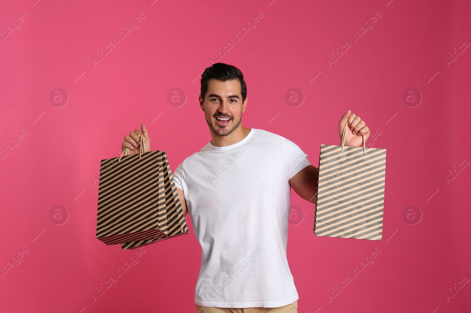 Photo of Young handsome man holding paper bags on pink background. Mockup for design