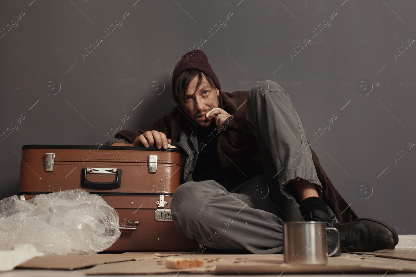 Photo of Poor homeless man eating on floor near dark wall