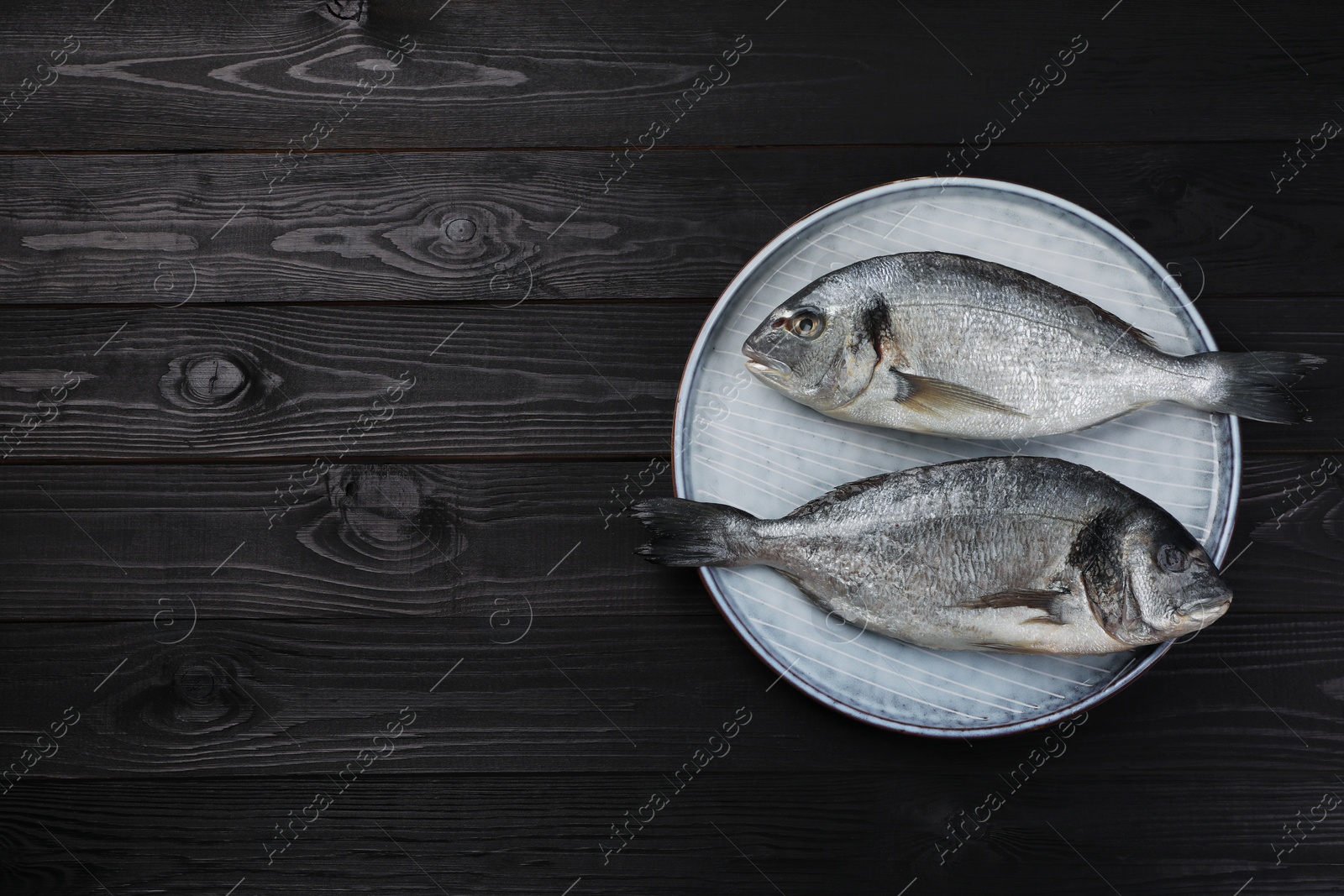 Photo of Fresh raw dorado fish on black wooden table, top view. Space for text