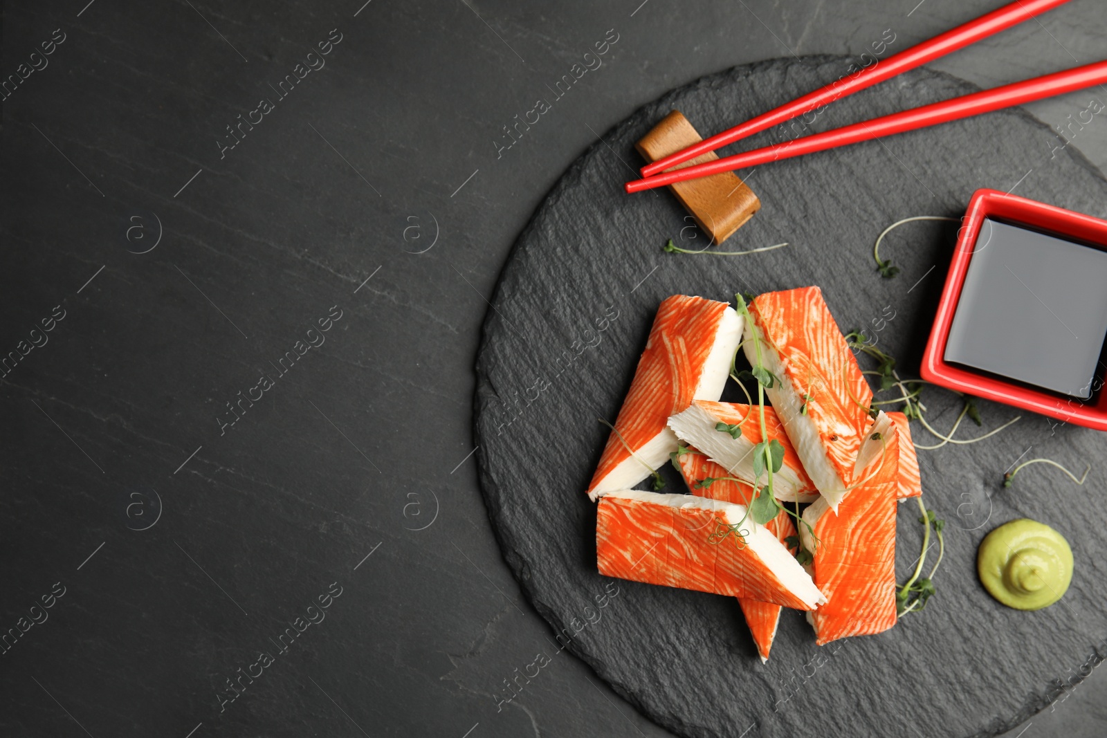 Photo of Fresh crab sticks with soy sauce served on black table, top view. Space for text