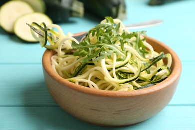 Photo of Delicious zucchini pasta with arugula in bowl on light blue wooden table, closeup