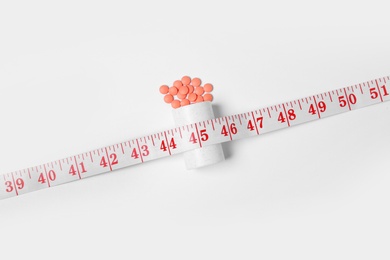 Weight loss pills and bottle with measuring tape on white background, top view