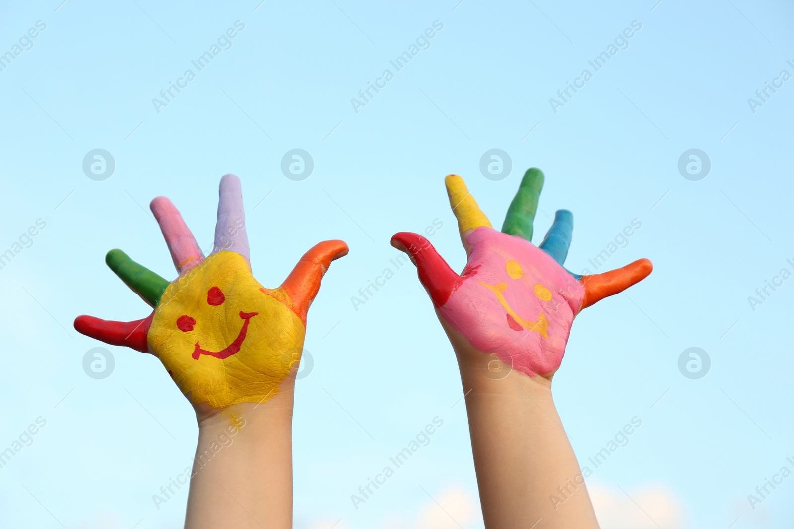 Photo of Kid with smiling face drawn on palms against blue sky, closeup