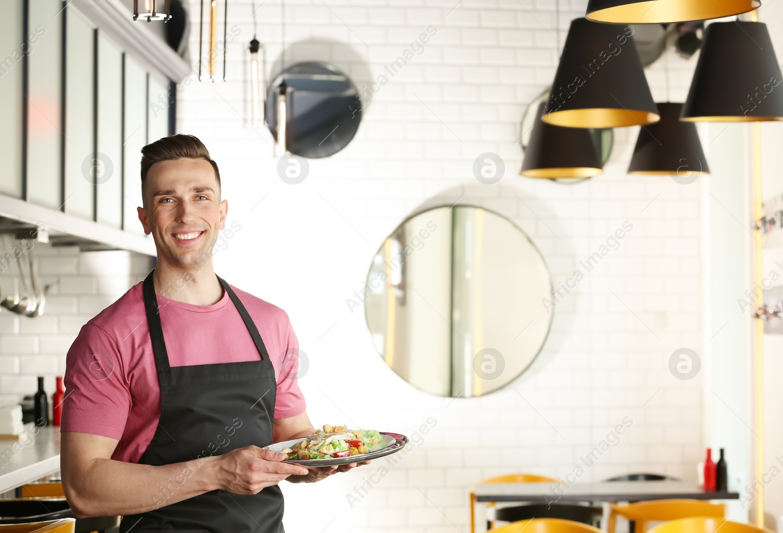 Photo of Young waiter in uniform holding tray with tasty dish at workplace