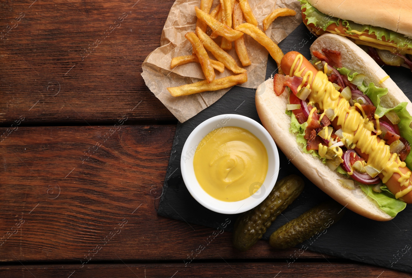 Photo of Delicious hot dogs with lettuce, onion and pickle served on wooden table, flat lay. Space for text