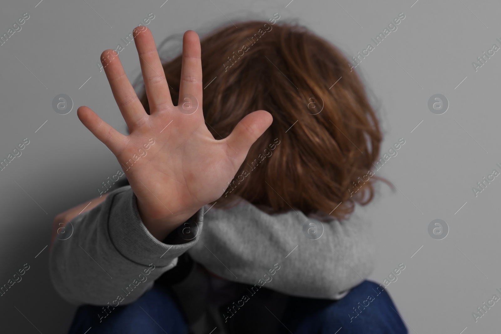 Photo of Child abuse. Boy making stop gesture near grey wall, selective focus