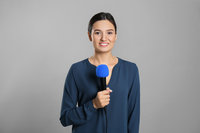 Photo of Young female journalist with microphone on grey background
