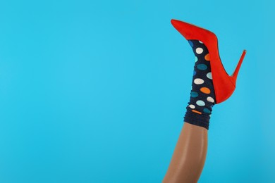 Photo of Woman wearing sock and high heel shoe on light blue background, closeup. Space for text