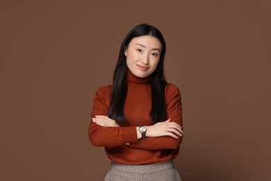 Portrait of beautiful woman with crossed arms on brown background