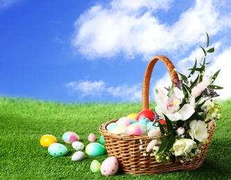 Image of Wicker basket with Easter eggs on green grass outdoors, space for text