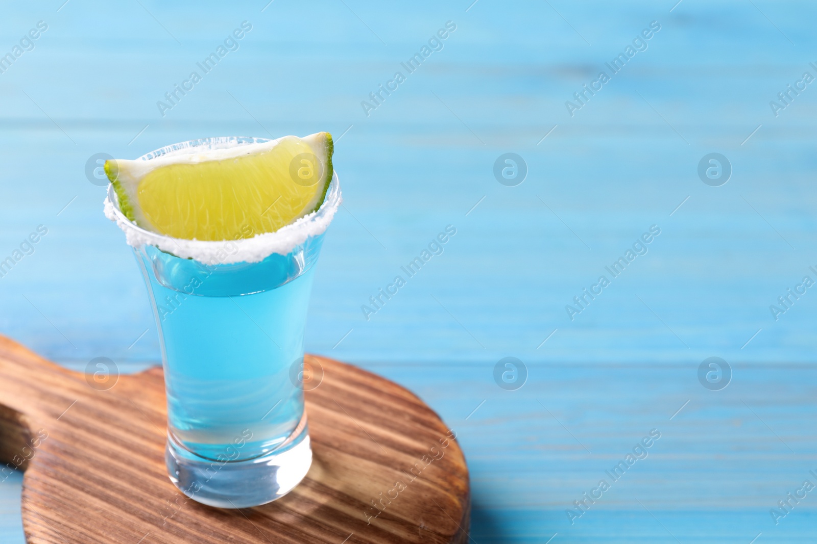 Photo of Light blue shot with lime on wooden table, space for text