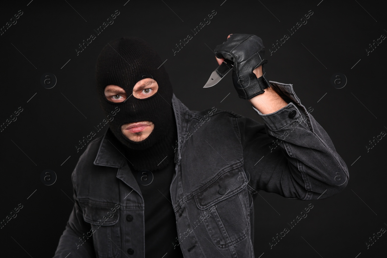 Photo of Man in mask with knife on black background. Dangerous criminal
