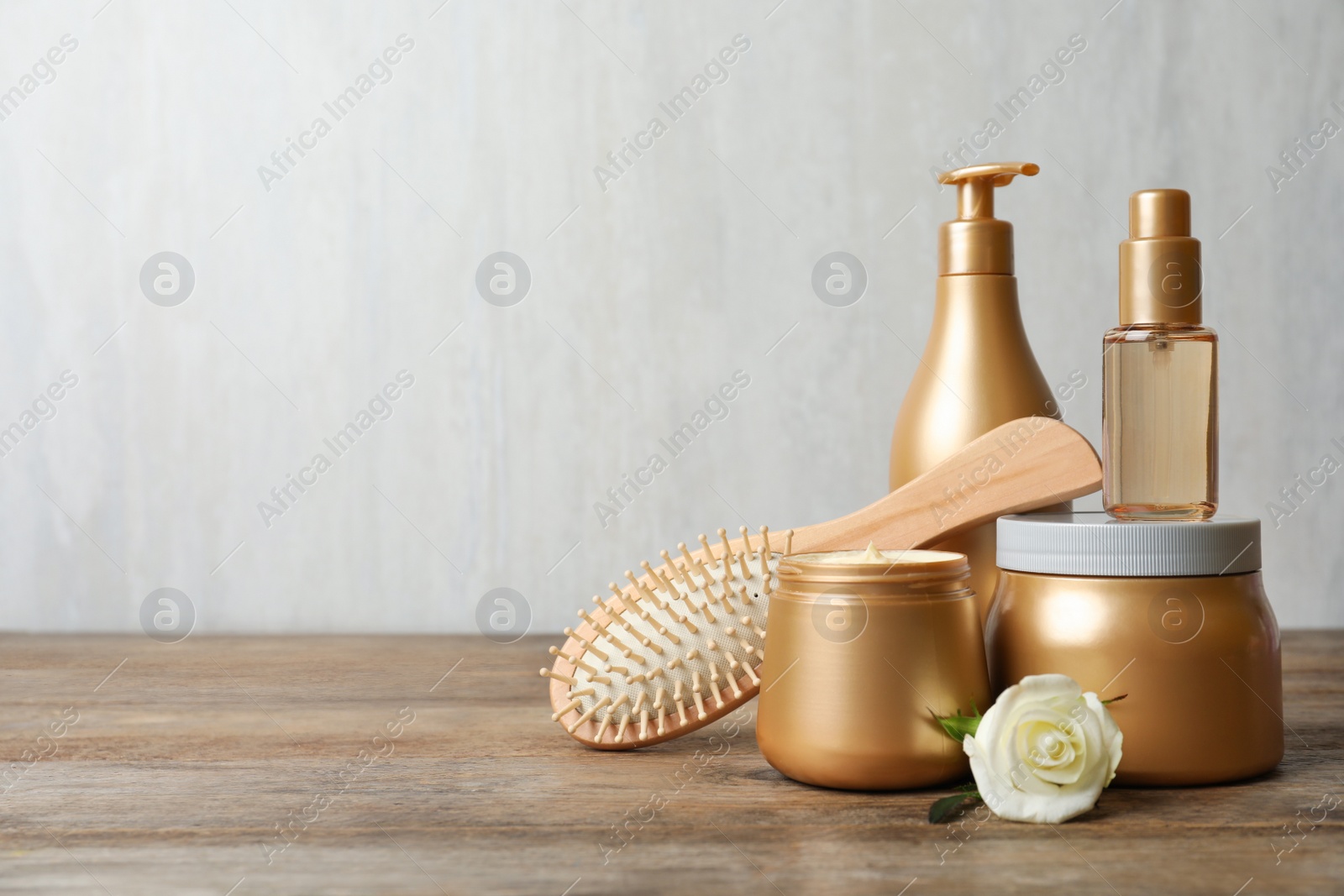 Photo of Different hair products, flower and brush on wooden table. Space for text