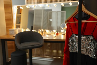 Photo of Makeup room. Chair near dressing table with stylish mirror indoors, focus on clothes rack