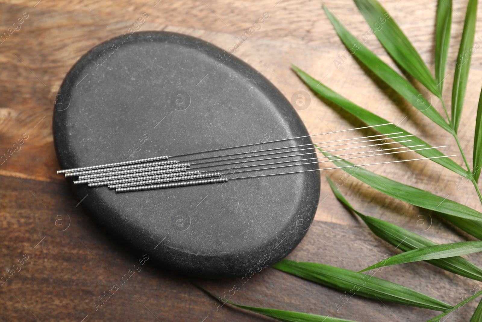 Photo of Acupuncture needles, spa stone and leaf on wooden table, flat lay