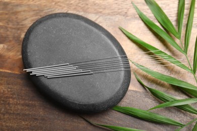 Acupuncture needles, spa stone and leaf on wooden table, flat lay