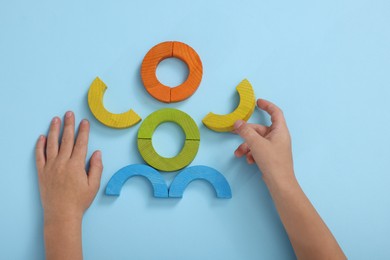 Photo of Motor skills development. Boy playing with colorful wooden arcs at light blue table, top view