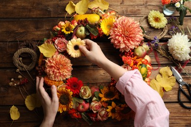Photo of Florist making beautiful autumnal wreath with flowers and fruits at wooden table, top view