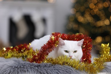 Photo of Cute cat with Christmas tinsel lying on fur rug in cosy room. Space for text