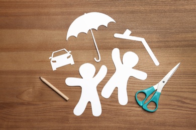 Photo of Flat lay composition with paper silhouettes of people with umbrella and scissors on wooden background. Life insurance concept