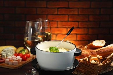 Photo of Fork with piece of broccoli, melted cheese in fondue pot, wine and snacks on table, closeup