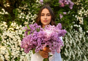 Photo of Attractive young woman with lilac flowers outdoors, focus on bunch