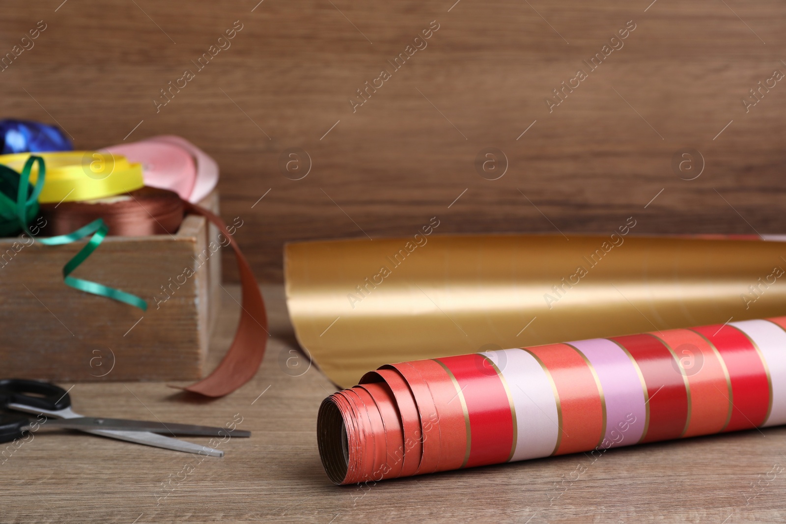 Photo of Roll of wrapping paper, scissors and ribbons on wooden table