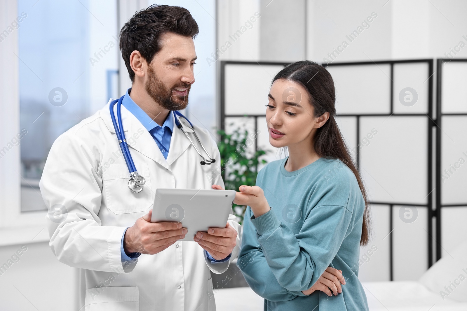 Photo of Doctor with tablet consulting patient during appointment in clinic