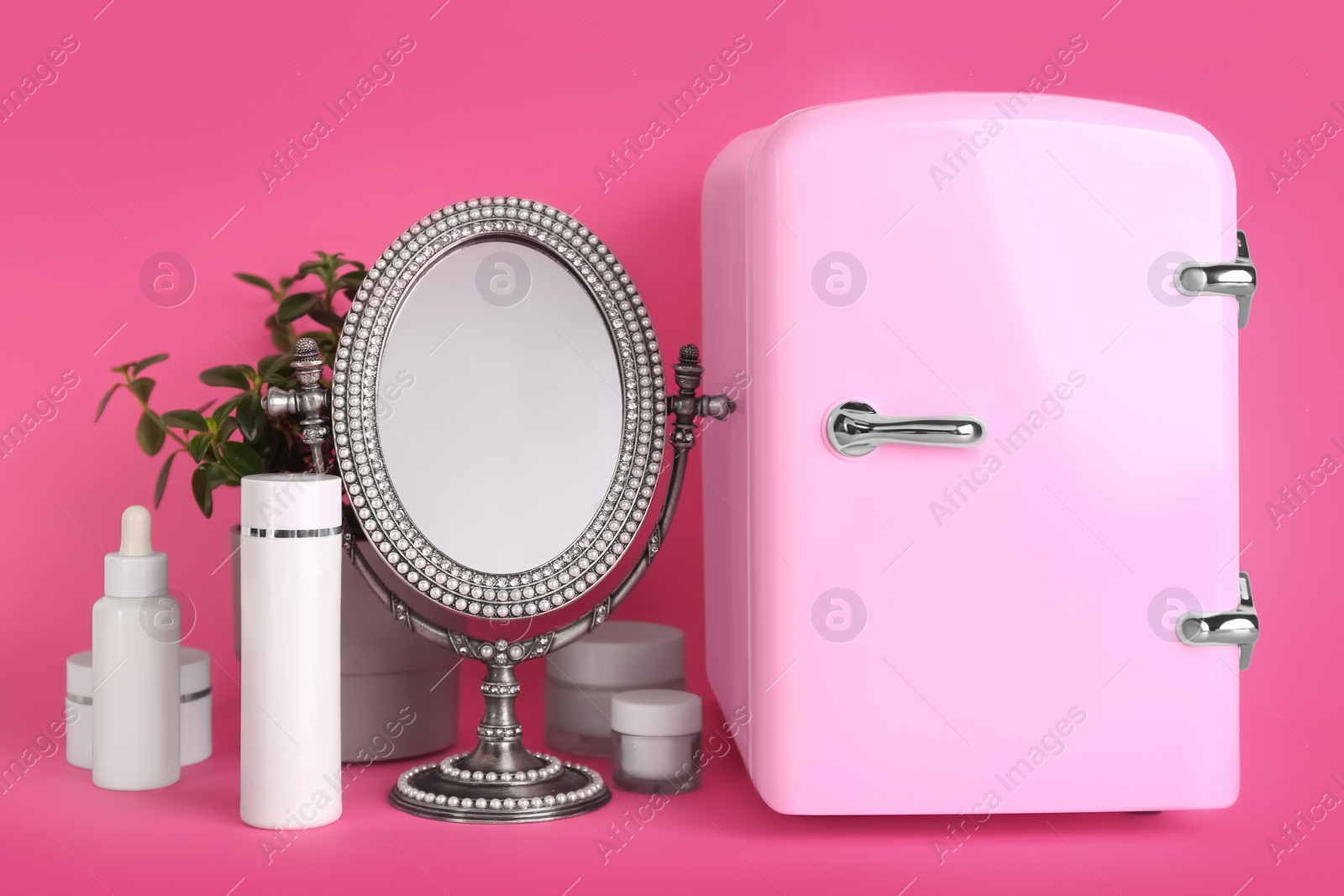 Photo of Cosmetic refrigerator and skin care products on pink background