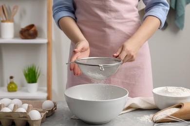 Photo of Making tasty baklava. Woman sifting flour into bowl at light grey marble table, closeup