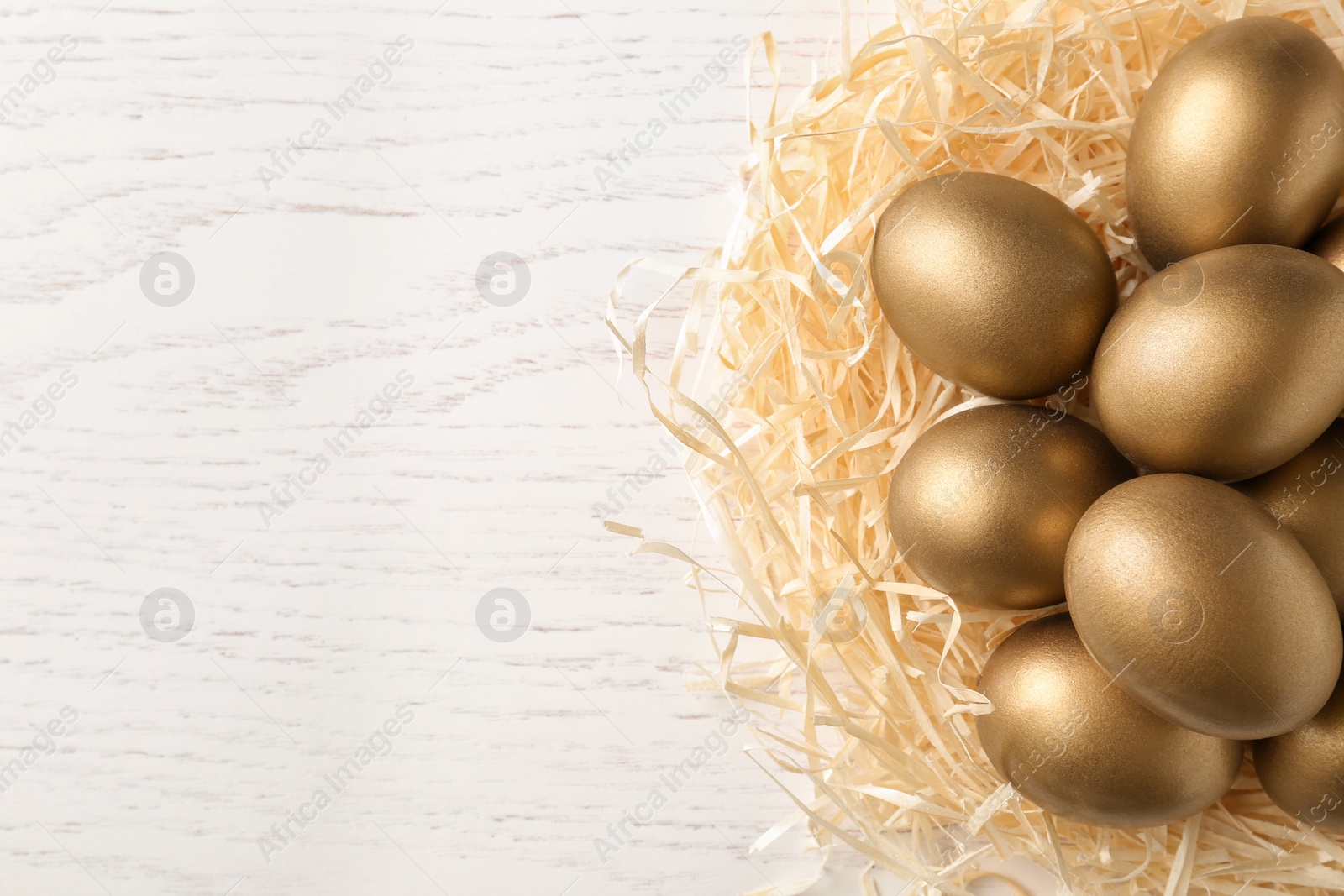 Photo of Golden eggs in nest on wooden background, top view with space for text