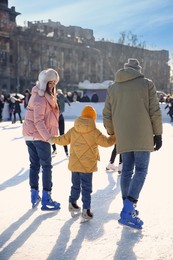 Image of Family spending time together at outdoor ice skating rink, back view