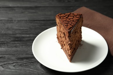 Photo of Piece of delicious chocolate truffle cake on black wooden table, closeup. Space for text