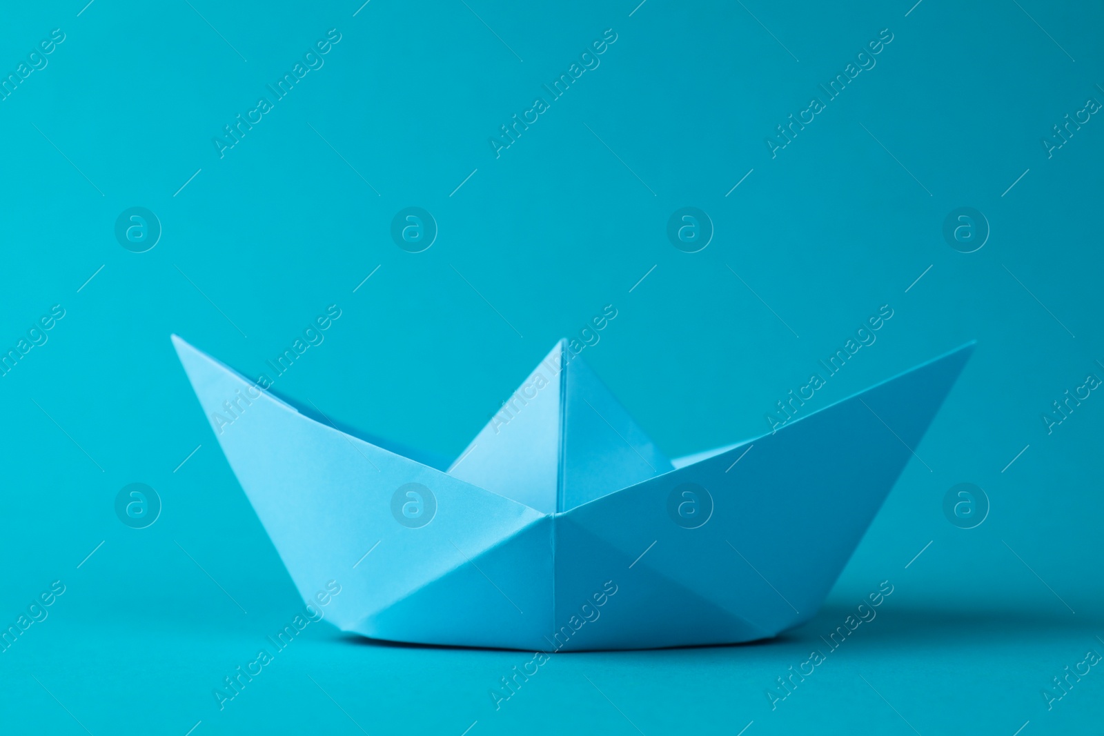 Photo of Handmade paper boat on light blue background. Origami art