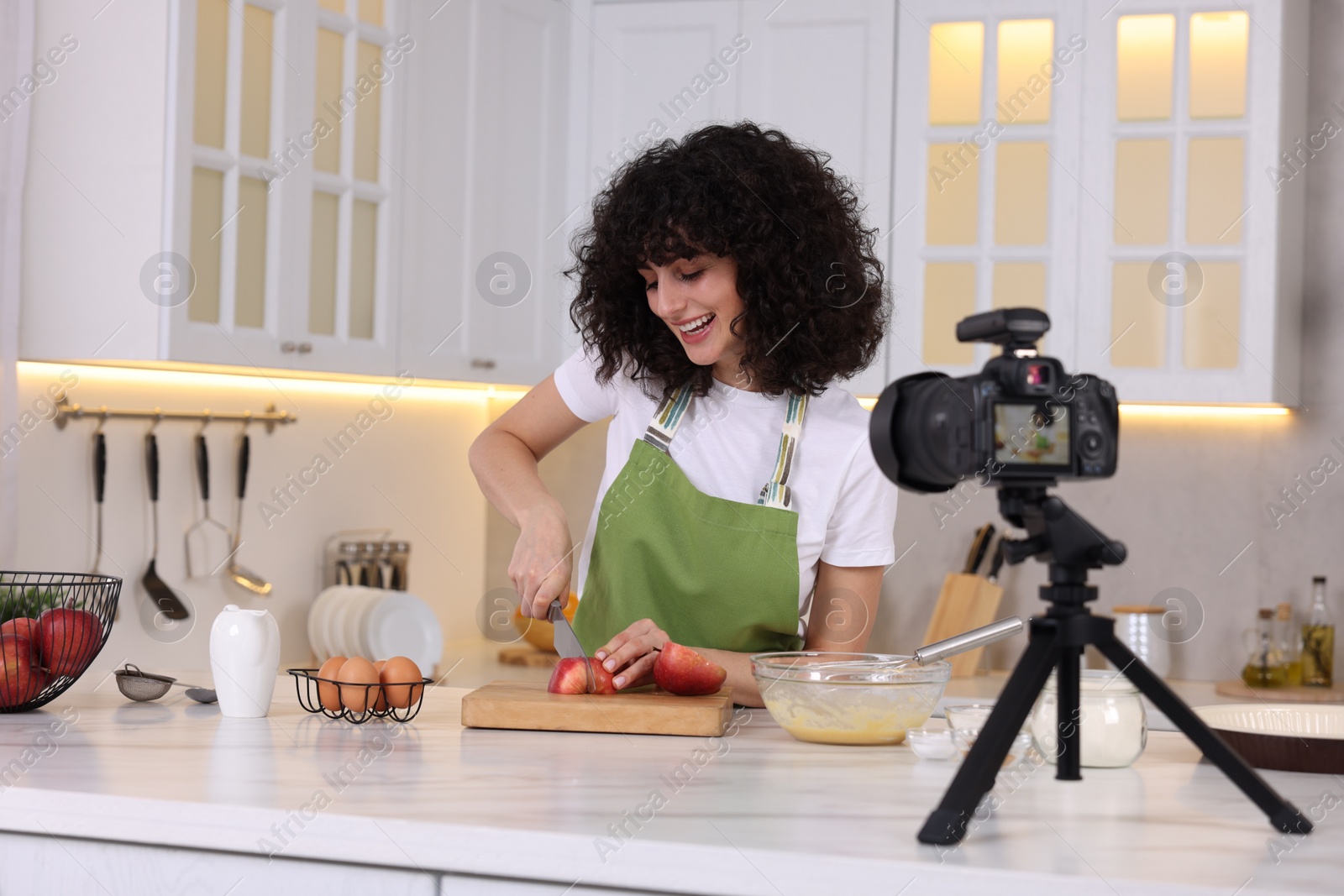 Photo of Smiling food blogger cooking while recording video in kitchen