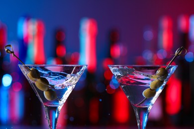 Photo of Martini glasses with splashing cocktail and olives in bar, closeup