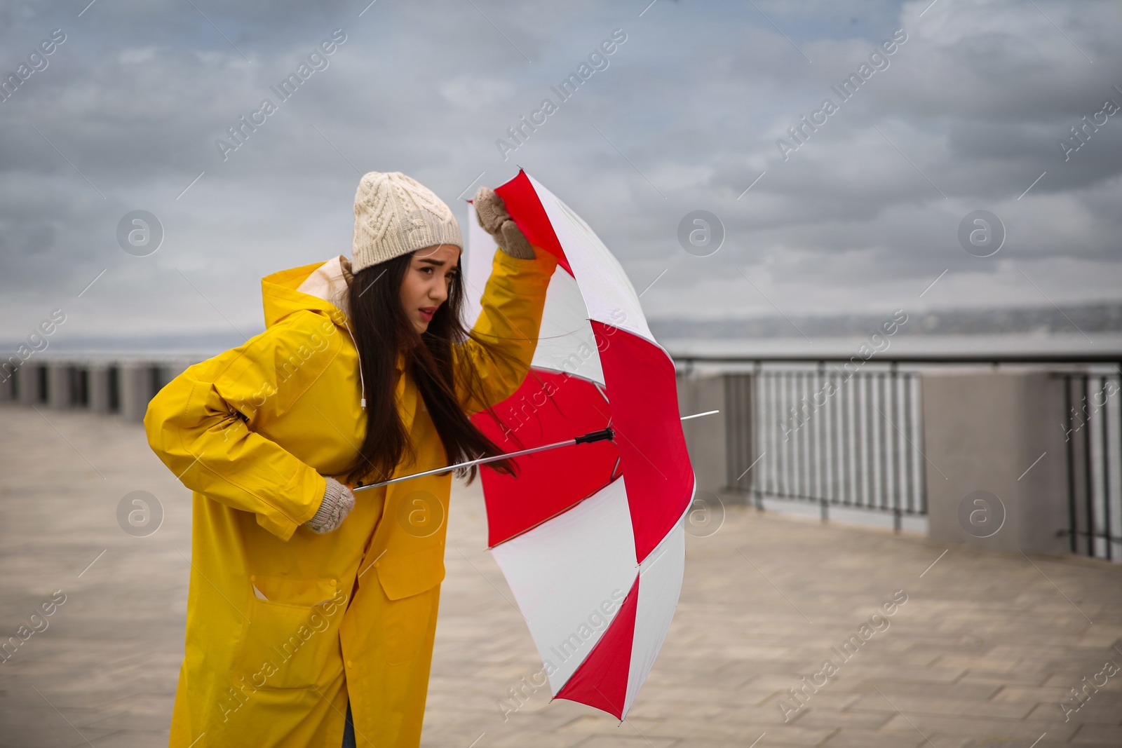 Photo of Woman in yellow raincoat with umbrella caught in gust of wind outdoors