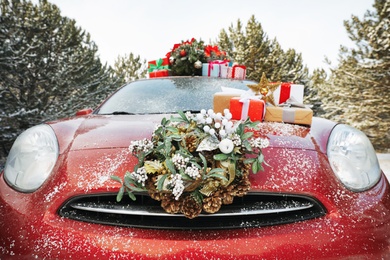 Photo of Car with Christmas wreath, tree and gifts in winter forest, closeup