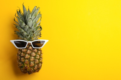 Photo of Pineapple with sunglasses on yellow background, top view. Space for text