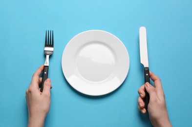 Photo of Woman with empty plate and cutlery on turquoise background, top view