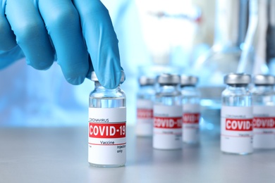 Doctor taking glass vial with COVID-19 vaccine from table, closeup