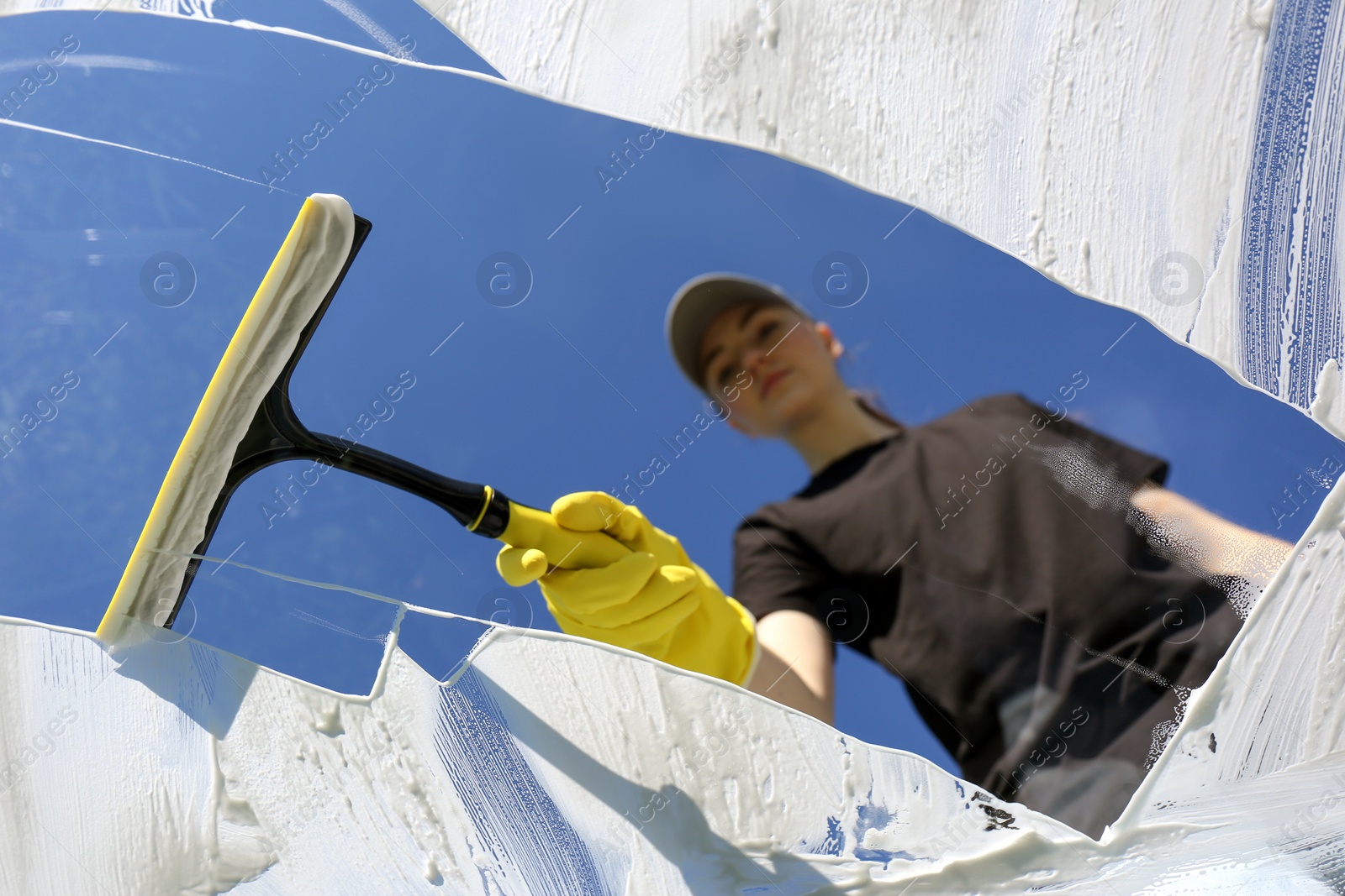 Photo of Woman cleaning glass with squeegee on sunny day