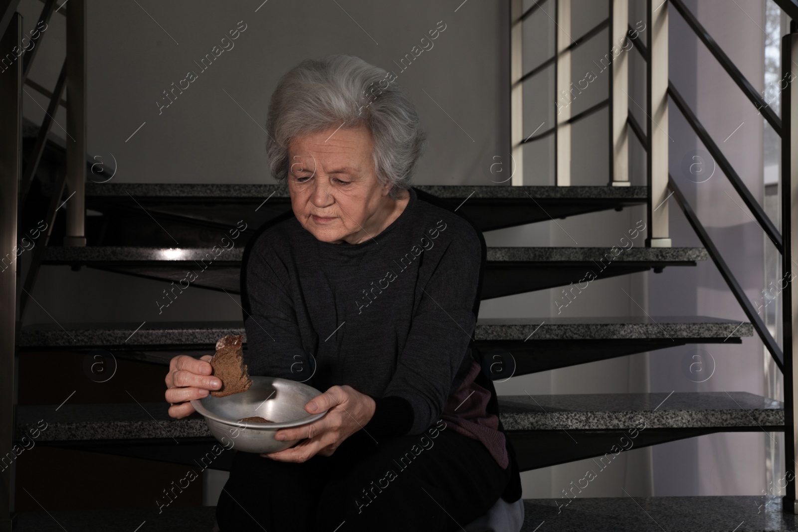 Photo of Poor mature woman with bowl and bread on stairs. Space for text