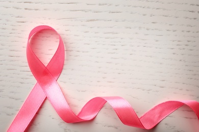 Pink ribbon on wooden background, top view with space for text. Breast cancer awareness concept