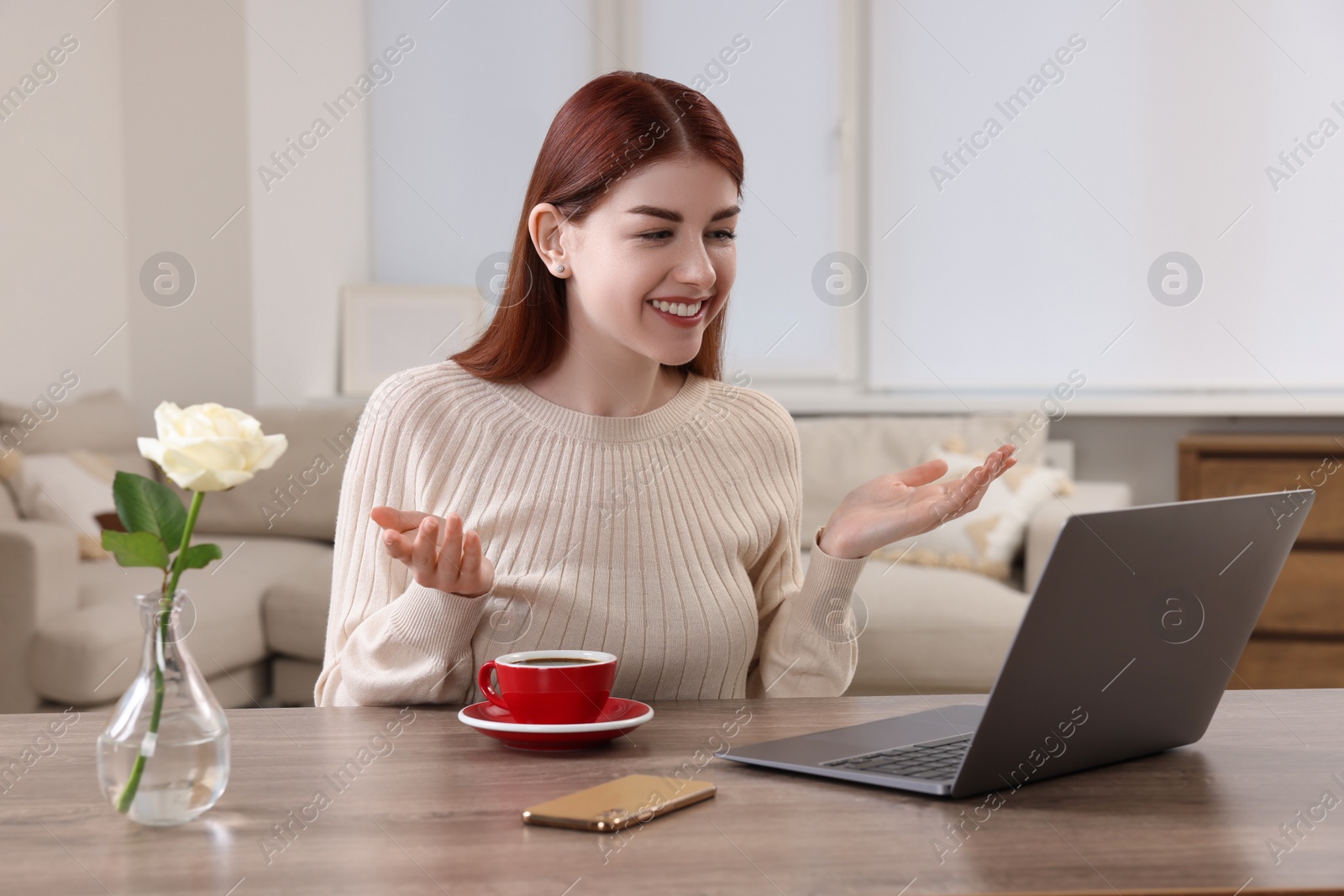 Photo of Happy woman having video chat via laptop at wooden table in room