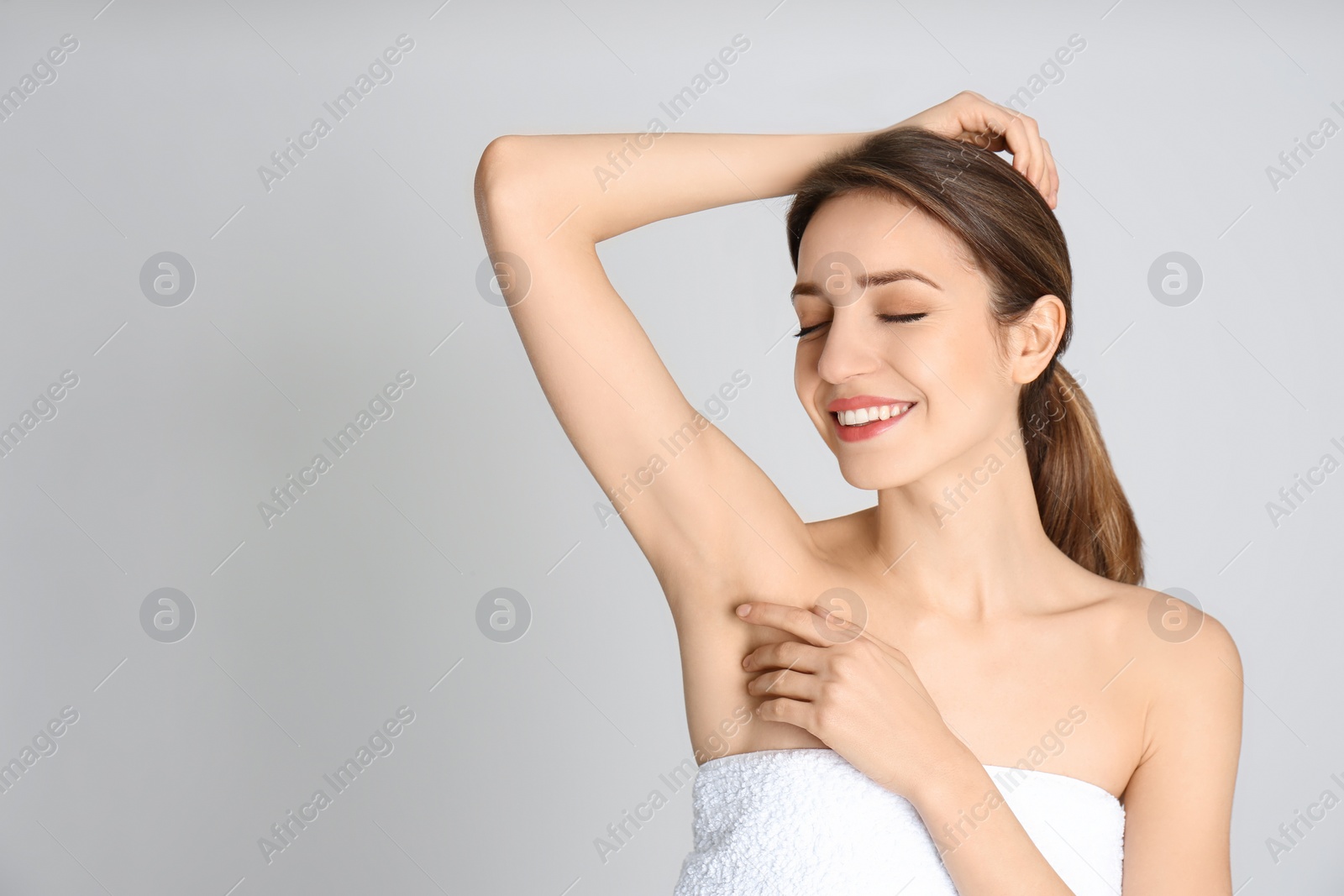 Photo of Young woman showing armpit with smooth clean skin on light grey background, space for text