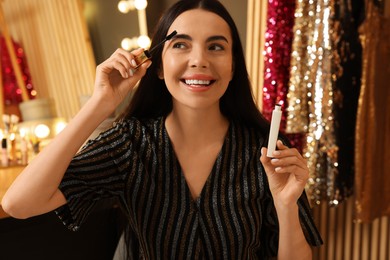 Beautiful young woman applying mascara in dressing room