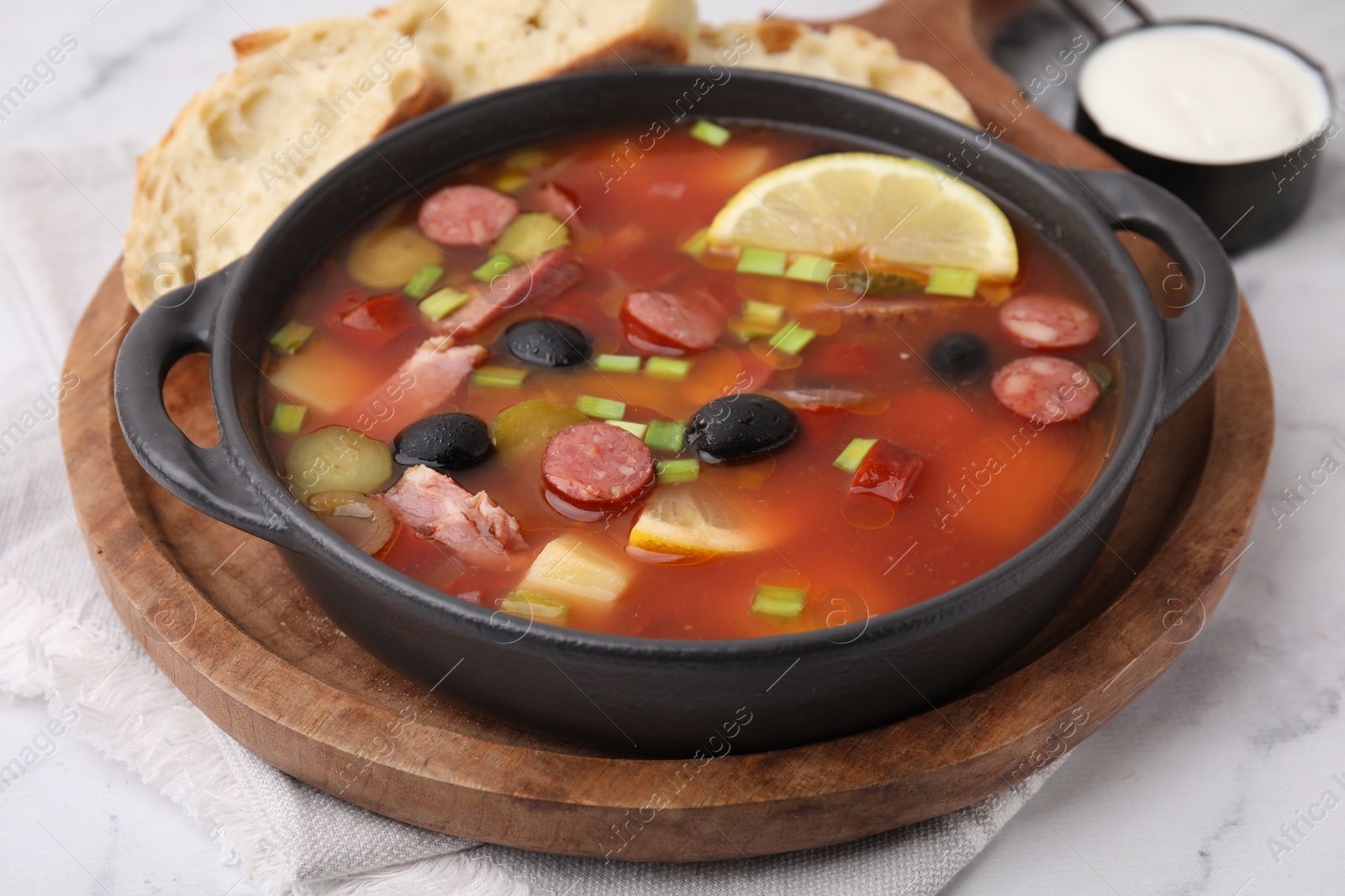 Photo of Meat solyanka soup with thin dry smoked sausages in bowl on white marble table