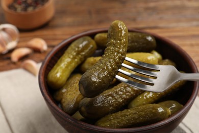 Fork with pickled cucumber over bowl on table, closeup