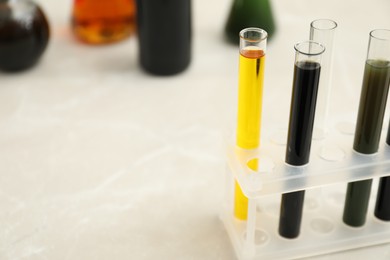 Test tubes with different types of crude oil on light marble table, space for text